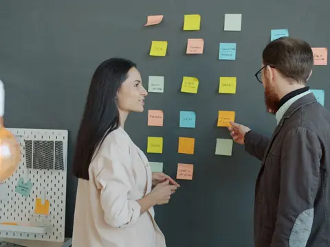 Two people arranging colored sticky notes on a studio wall