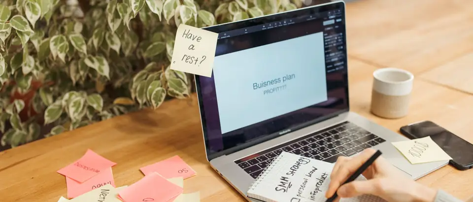 A woman writing a plan on sticky notes beside a laptop on a wooden table