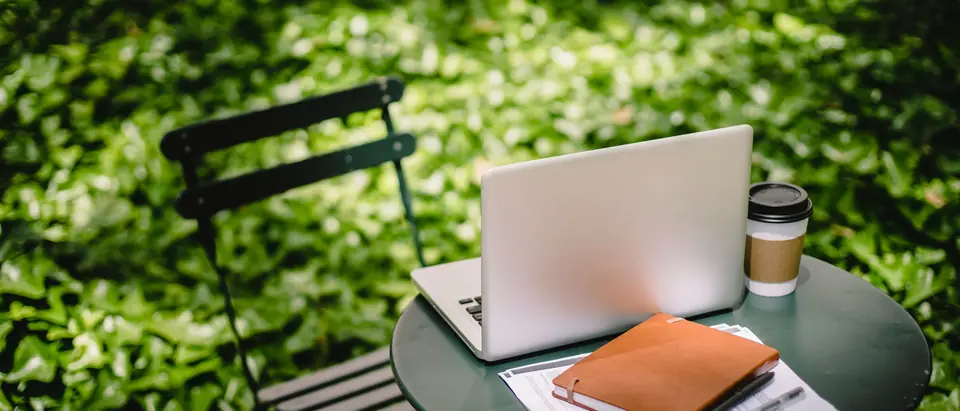 A laptop, notebook and coffee on a round table in a sunny garden