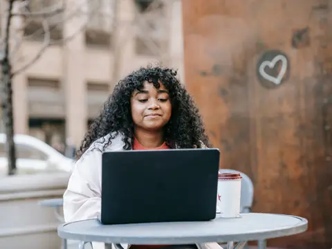 A woman smiling as she works on a laptop at an outdoor table
