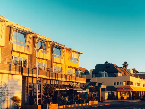 A row of sunlit shops and cafes along a seaside street