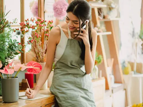 A florist on a phone call at the counter of her bright flower shop