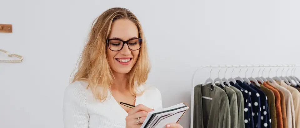 A woman taking notes in a notebook in her bright clothing studio