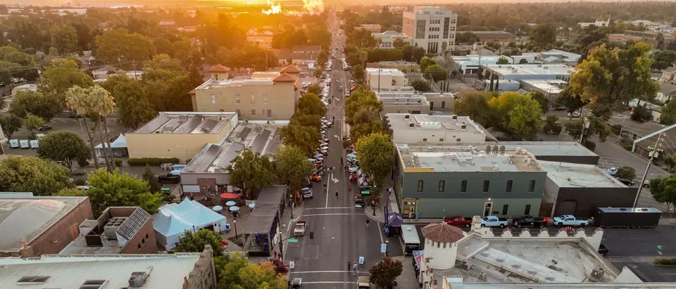 A tree-lined main street of local shops and offices seen from the air at sunset