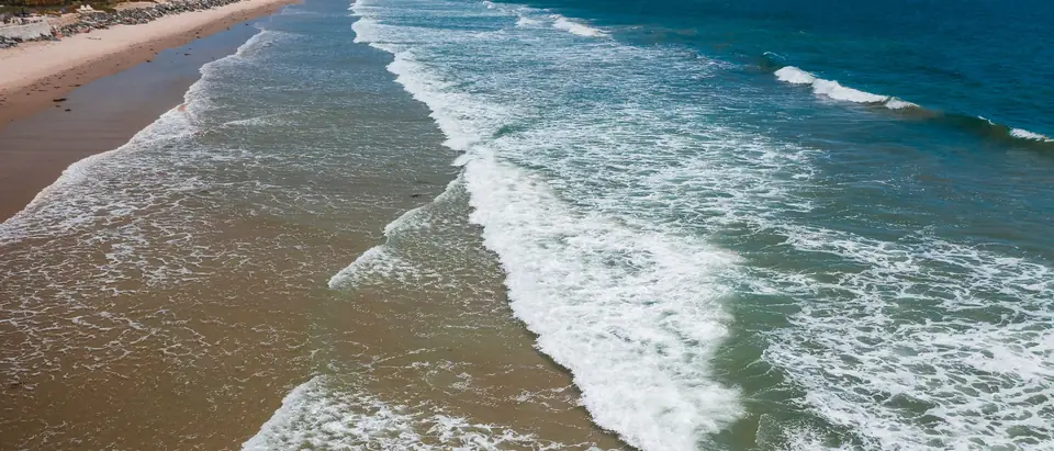 Waves rolling onto a long sandy beach below a coastal town, seen from the air