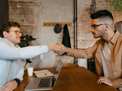 Two men shaking hands across a table in a bright office