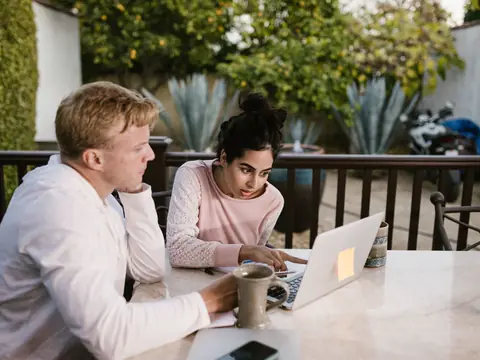 Two people talking over a laptop at an outdoor terrace table