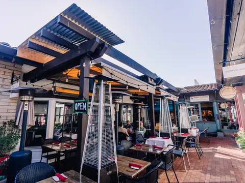 Diners at tables on a sunny restaurant patio under an open pergola