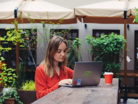 A woman working on a laptop at a sunny garden cafe table