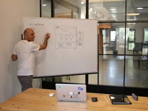 A man sketching website page layouts on a whiteboard in a bright office