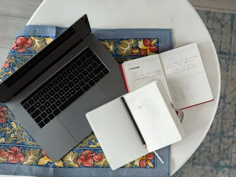 An open laptop and two notebooks on a round cafe table