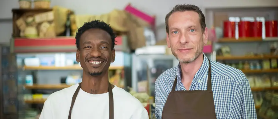 Two smiling shop owners in aprons inside their store