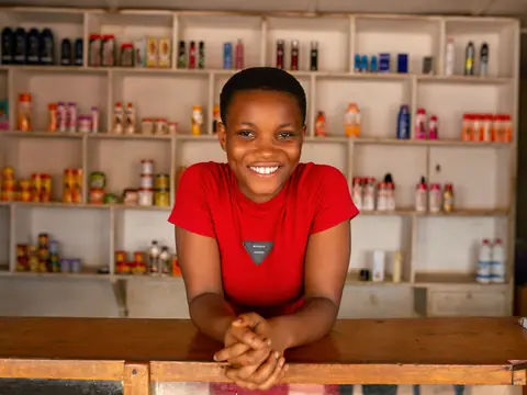 A smiling shop owner leaning on her counter in front of stocked shelves
