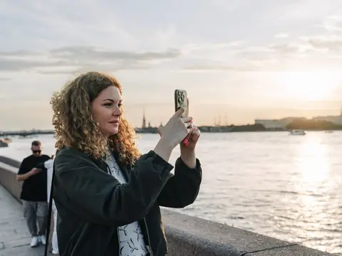 A woman recording a video on her phone by the water at sunset