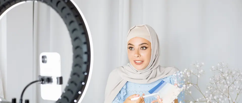 A woman recording a video with a phone and a ring light at a bright table